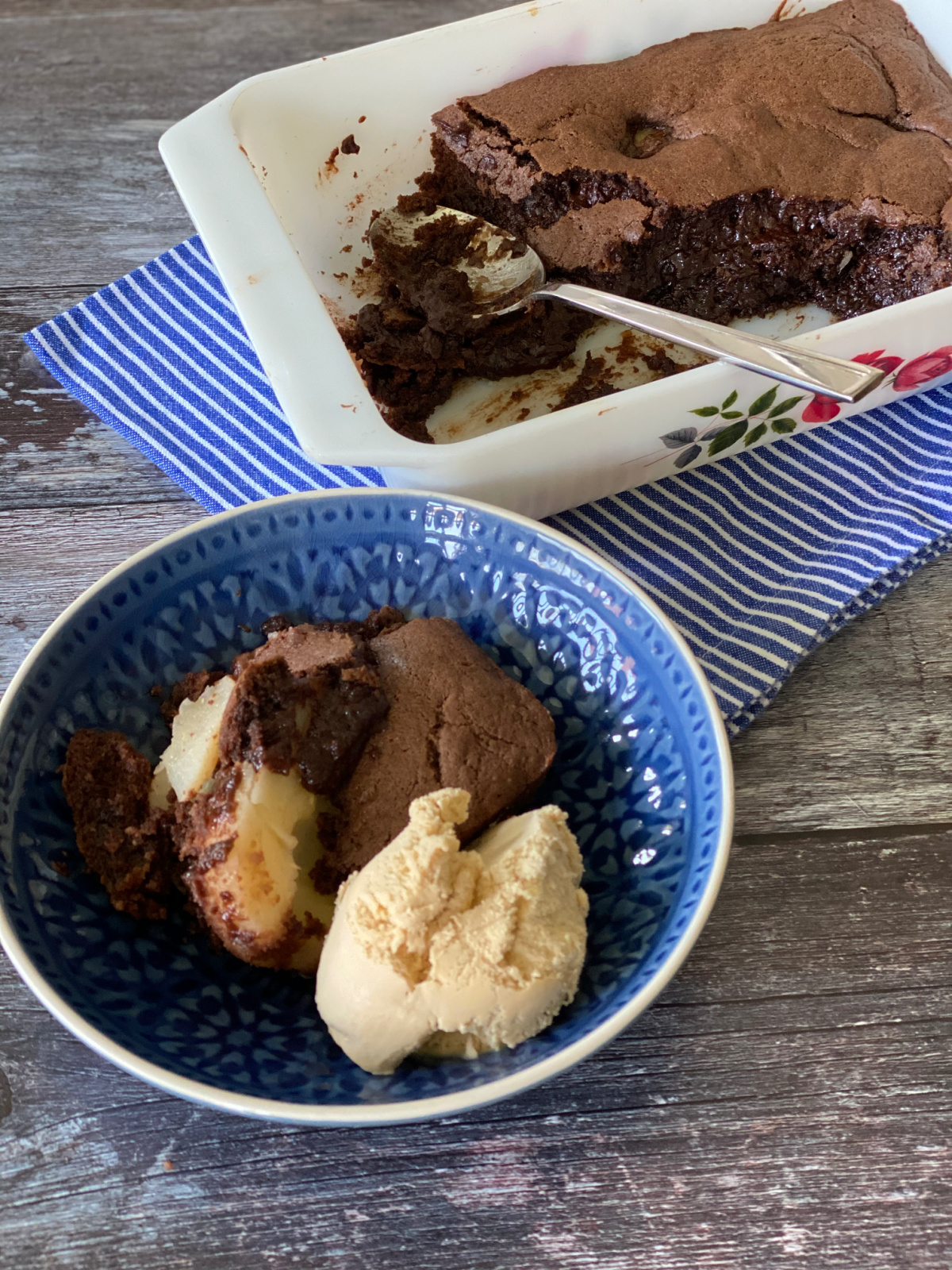 Chocolate and Pear Pudding Cake in a casserole dish with a serving of the cake in a blue bowl in the foreground