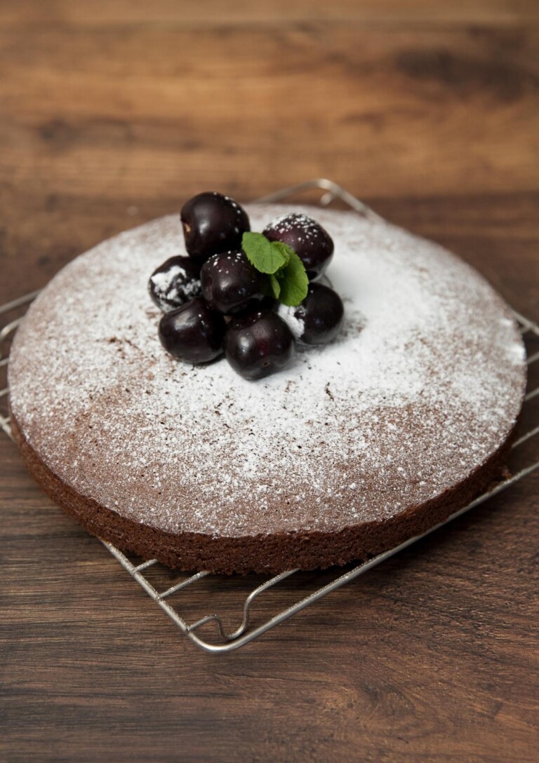 Easy Chocolate Cake sprinkled with icing sugar and topped with cherries