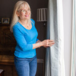 April Harris at a window, pulling back the curtains - feathering an empty nest