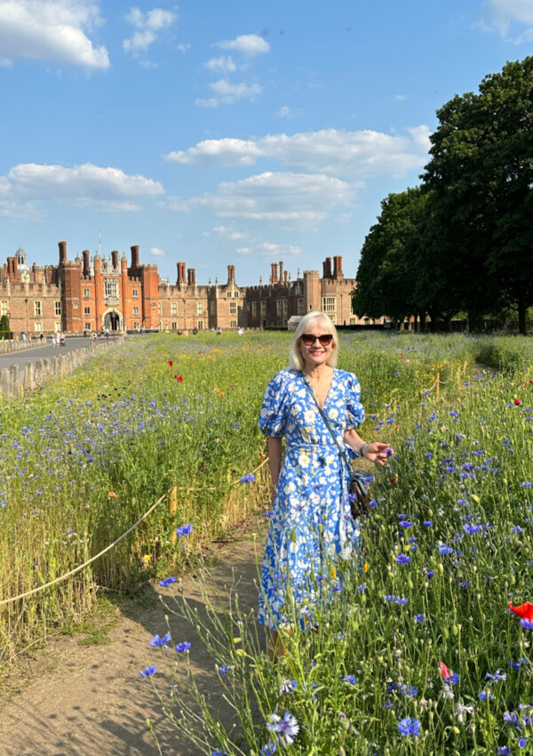 April Harris wearing a blue patterned dress in the wildflower meadow in front of Hampton Court Palace
