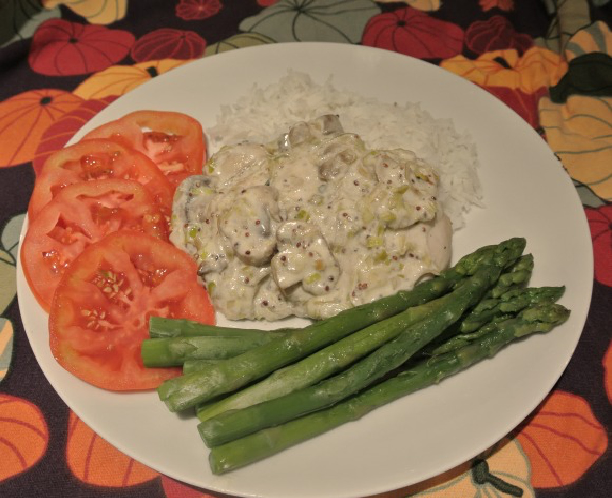 Chicken in a Leek Mushroom and Wholegrain Mustard Sauce served on a white plate with tomatoes and asparagus