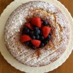 An Easy Almond Cake served on a white plate. The cake is a Bundt cake and there are strawberries and blueberries in the centre.