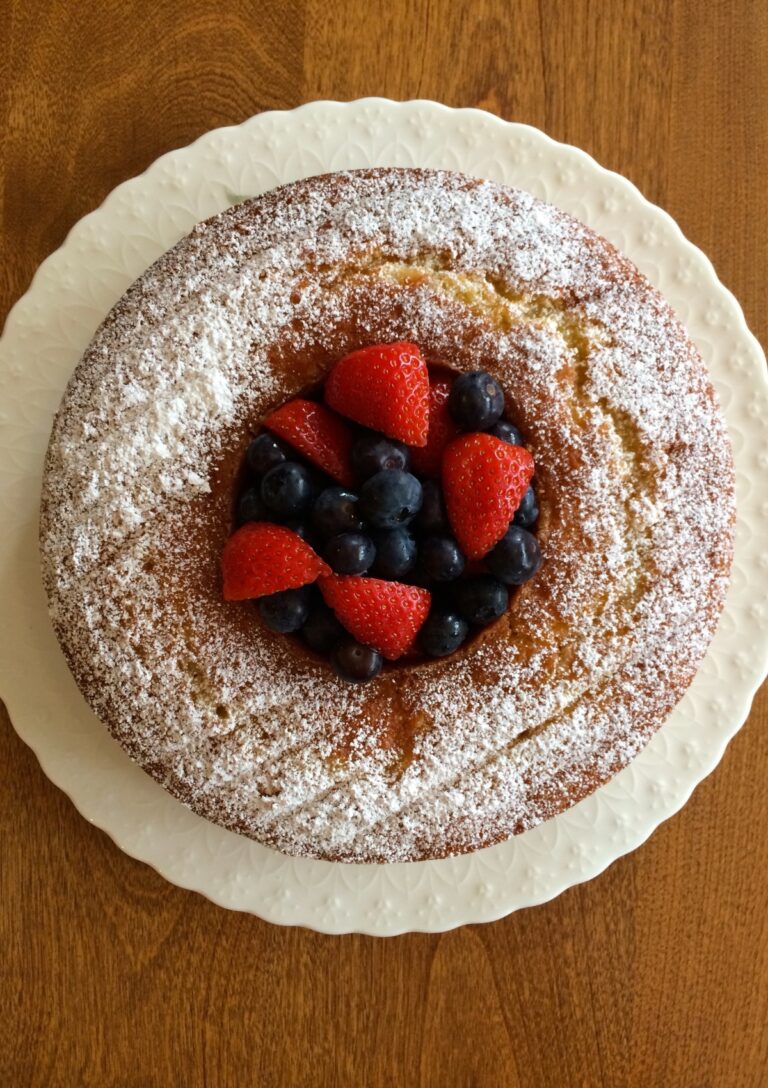 An Easy Almond Cake served on a white plate. The cake is a Bundt cake and there are strawberries and blueberries in the centre.
