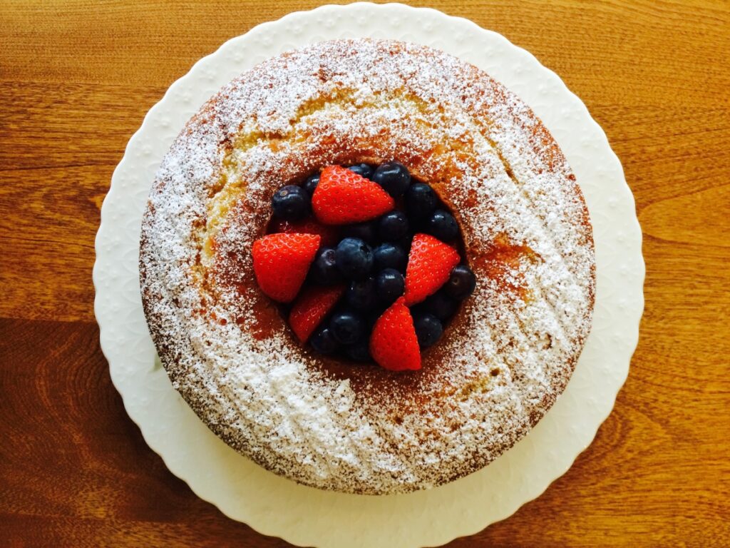 Easy Almond Cake served on a white plate. This hole in this Bundt-style cake is filled with berries.