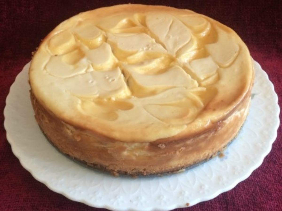 A Baked Lemon Cheesecake with lemon curd swirls served on a white cake plate