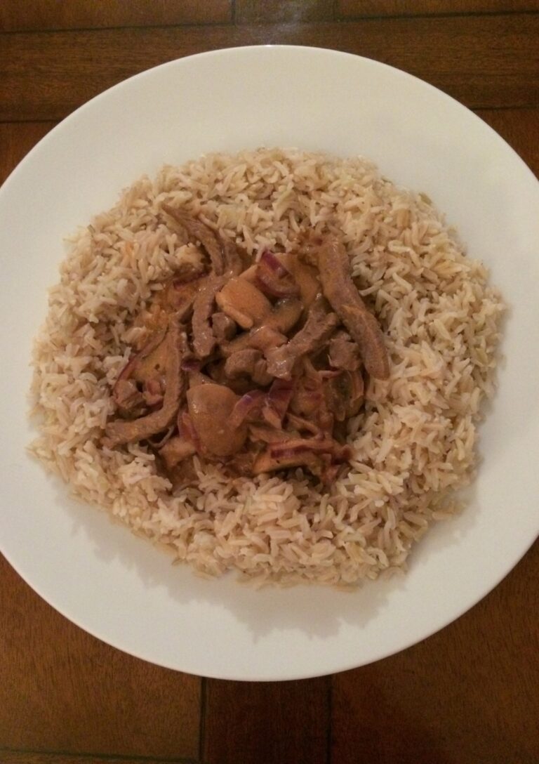 Lighter Beef Stroganoff served over brown rice on a white plate