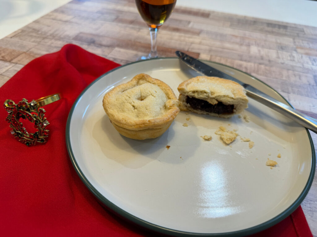 Two mincemeat pies won a white plate. One of the pies is sliced in half so you can see the filling