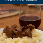 Pinterest Pin image with words for Poor Man's Steak Diane. The recipe is pictured served over mashed potatoes on a white plate with a glass of red wine in the background