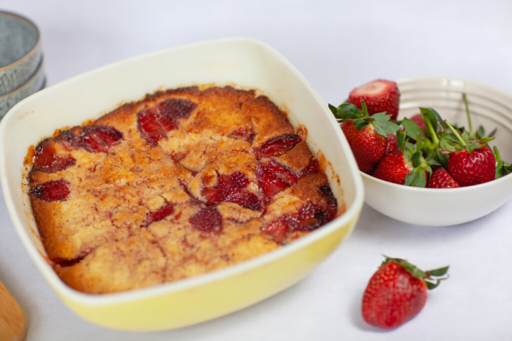 Strawberry Pudding Cake in a vintage yellow casserole dish with a bowl of strawberries alongside