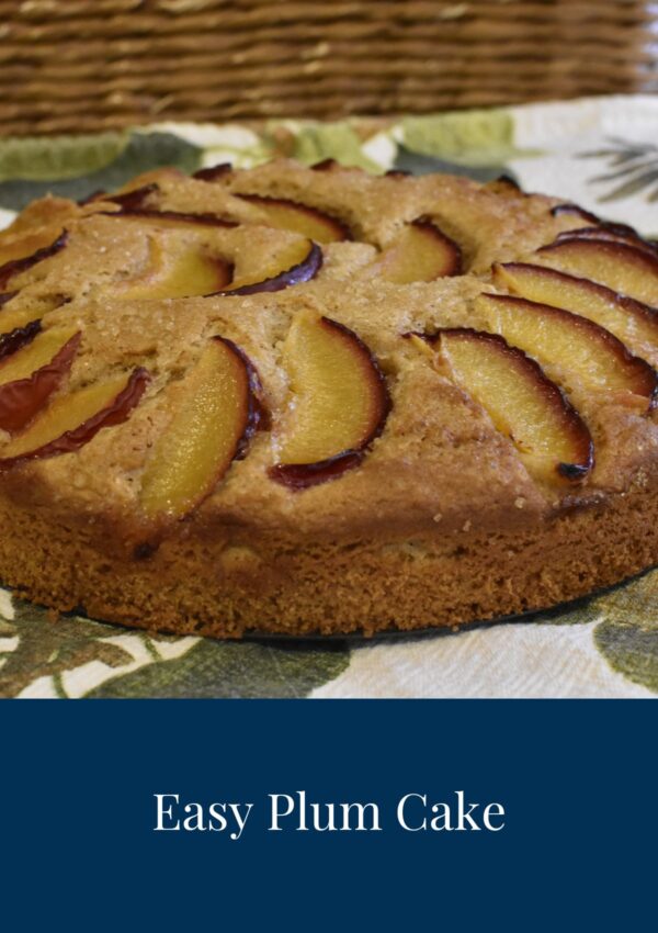 A whole Easy Plum Cake sat on a tea towel with a leaf pattern