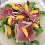 Peach and Proscuitto Salad with Parmesan served on a large white plate with a blue border