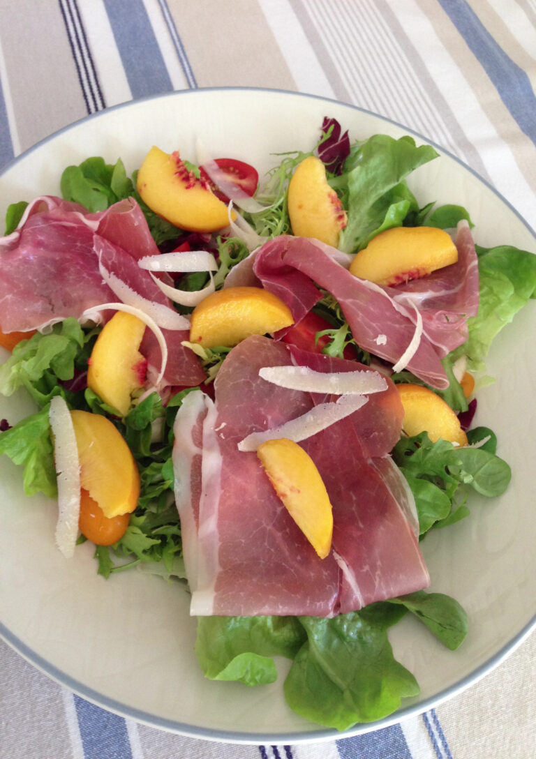 Peach and Proscuitto Salad with Parmesan served on a large white plate with a blue border