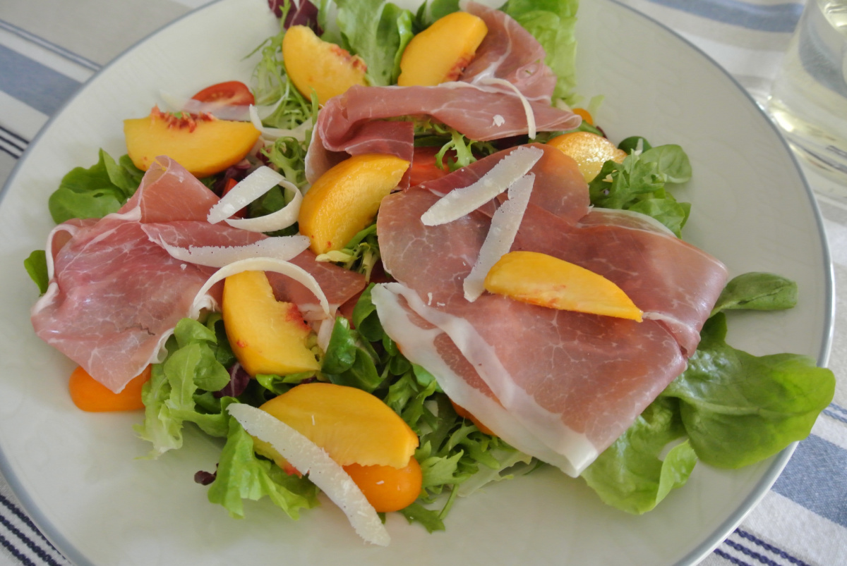 Peach and Proscuitto Salad with Parmesan served on a large white plate with a blue border