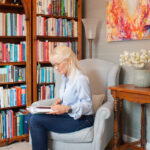April J Harris sitting on a chair and reading a book in her library at home