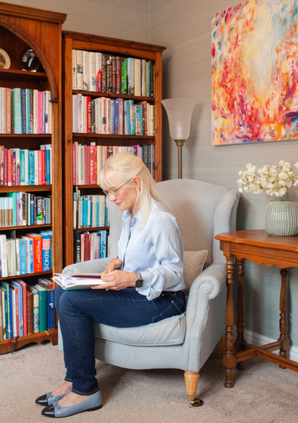 April J Harris sitting on a chair and reading a book in her library at home