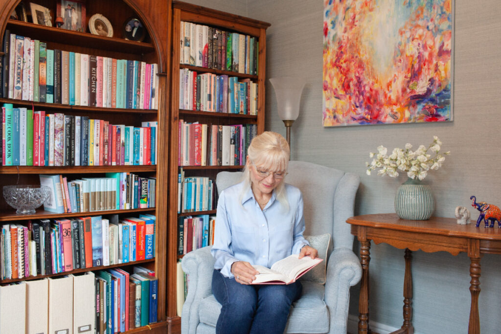 April J Harris sitting on a chair reading a book in her library at home
