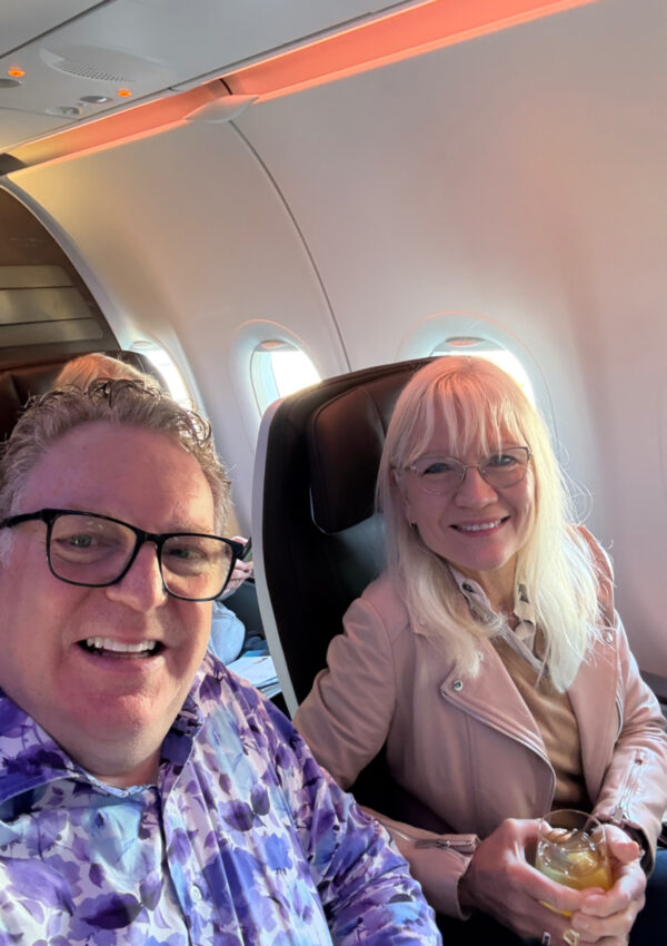 Guy and April Harris in First Class on Hawaiian Airlines. April is holding a glass of sparkling water.