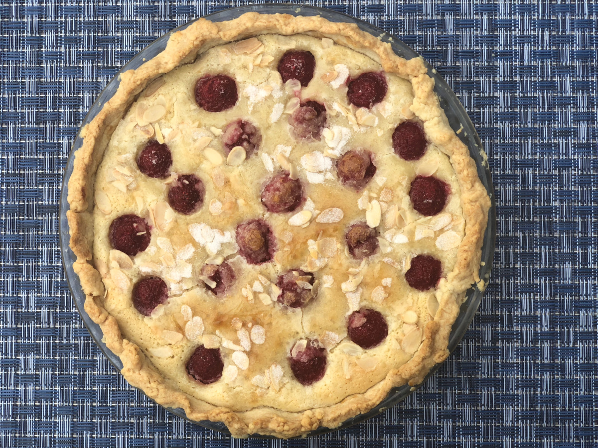 A whole Raspberry Almond Tart sitting on a blue placemat