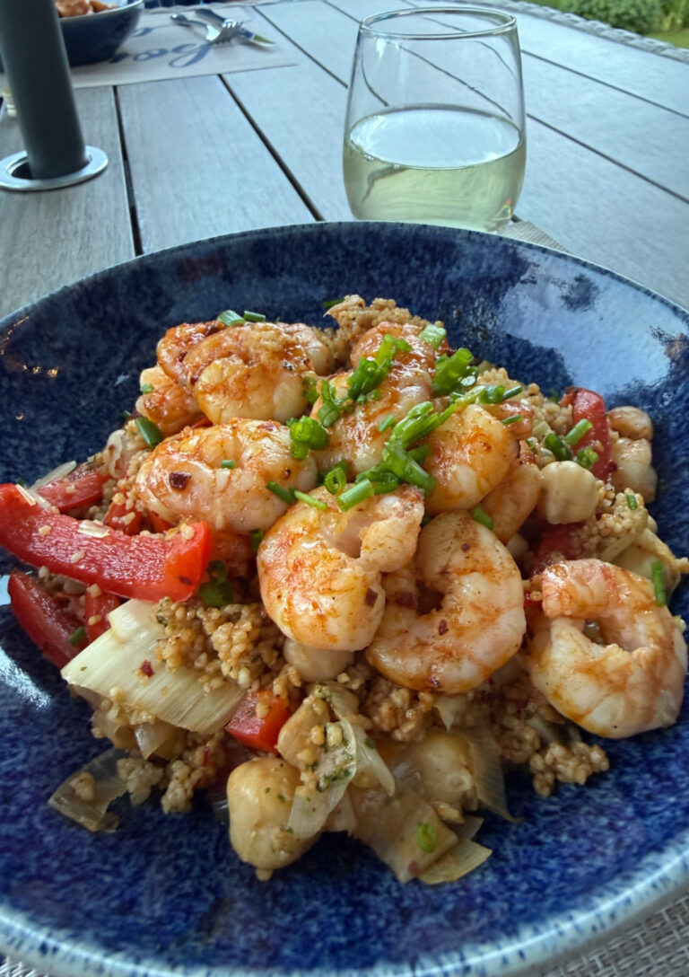 Moroccan Shrimp and Couscous served in a blue bowl with a glass of white wine alongside.