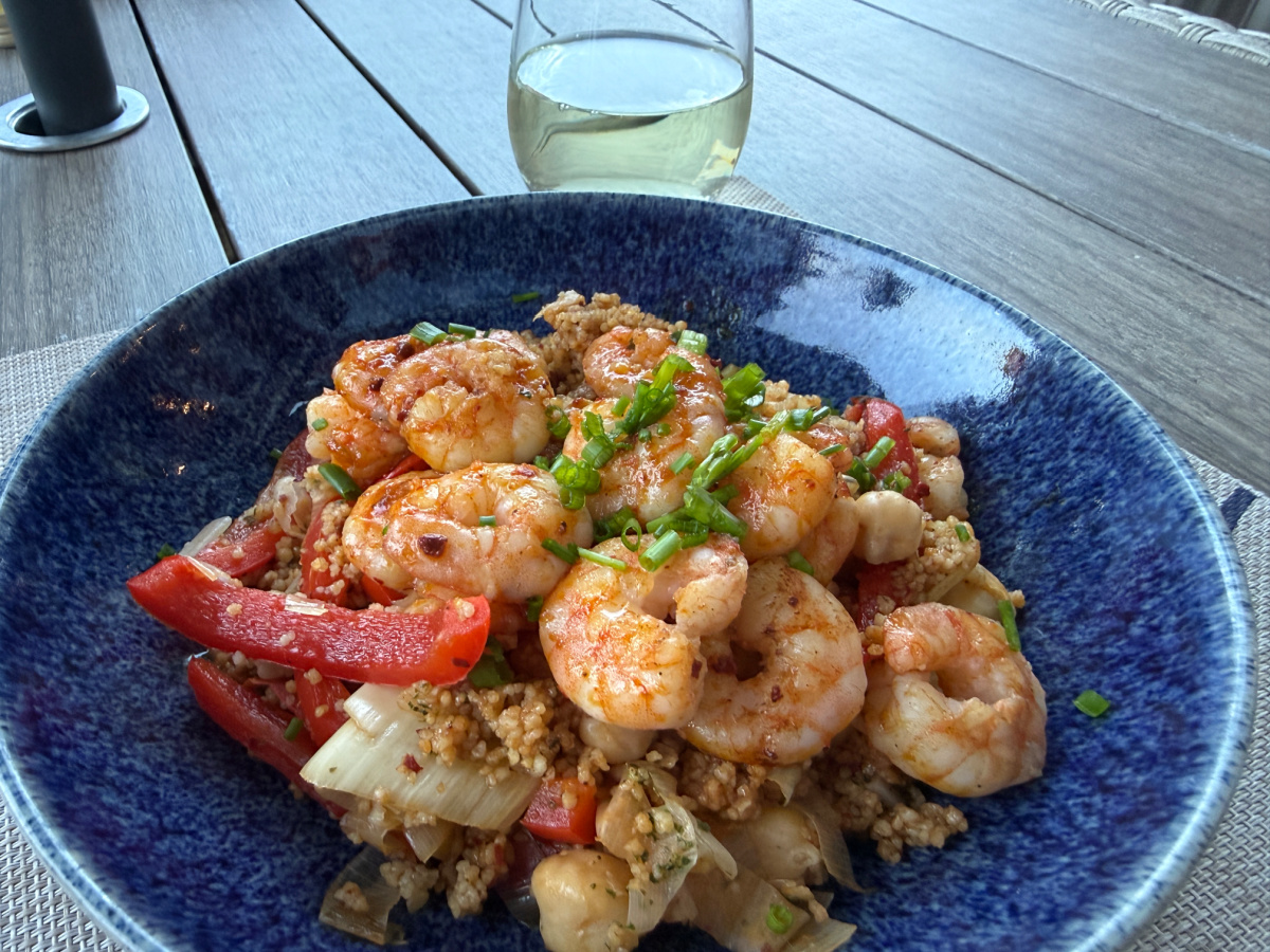 Moroccan Shrimp and Couscous served in a blue bowl with a glass of white wine alongside.