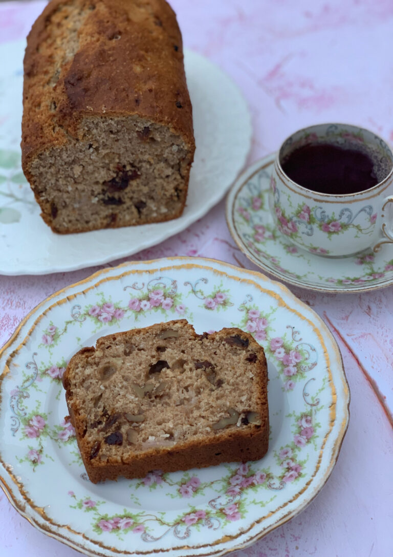 Banana Maple Walnut Loaf in the background with a slice in the foreground. There is a cup of tea on the right hand side.
