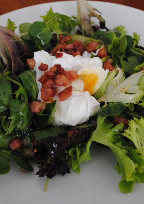 Salade Frisée aux Lardons with crispy bacon lardons, tangy greens and a poached egg served on a plate