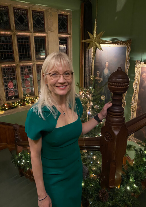 April J Harris in a green dress on a staircase. The top of a Christmas tree is visible in the background.