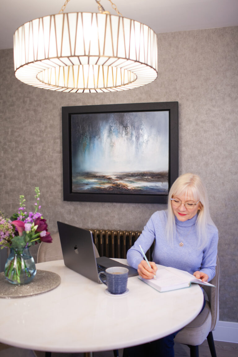 April J Harris image for how to make resolutions that work - April is sitting at a table writing in a notebook