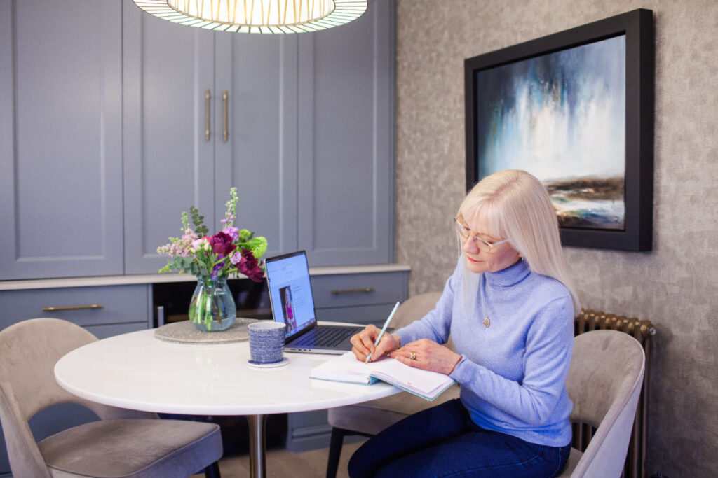 April J Harris image for how to make resolutions that work - April is sitting at a table writing in a notebook