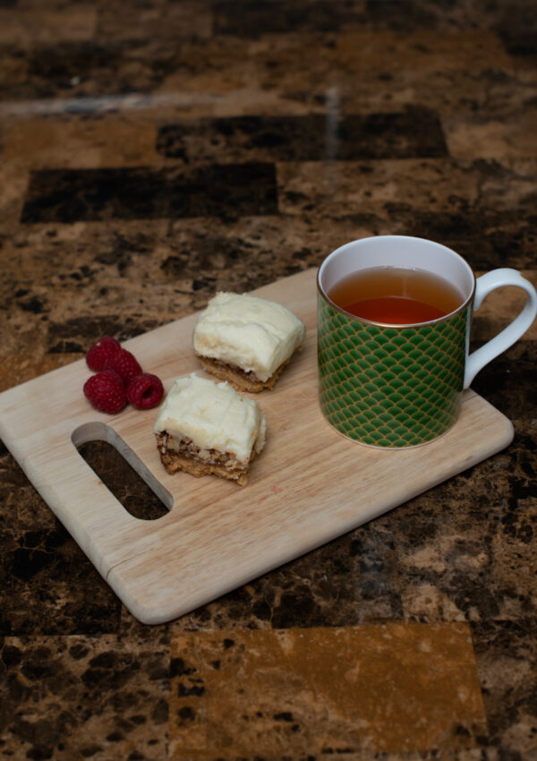 Lemon and Walnut Squares served on a breadboard with a raspberry garnish and a cup of tea