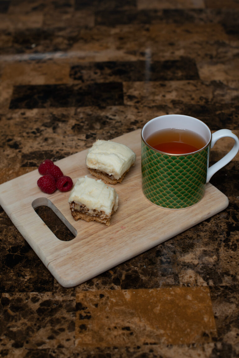 Lemon and Walnut Squares served on a breadboard with a raspberry garnish and a cup of tea
