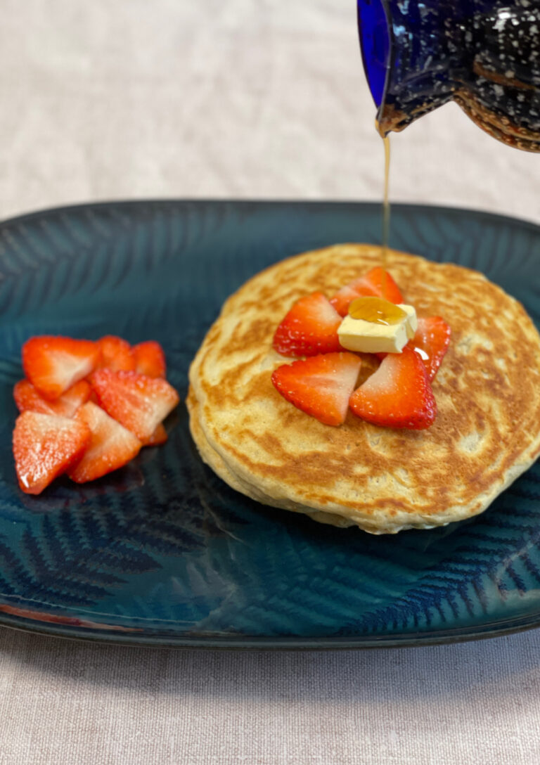 Strawberry Flavoured pancakes with sliced strawberries on top and on the side having some syrup poured over