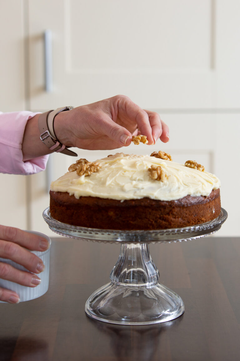 Old Fashioned Banana Cake on a raised cake stand being decorated with walnuts