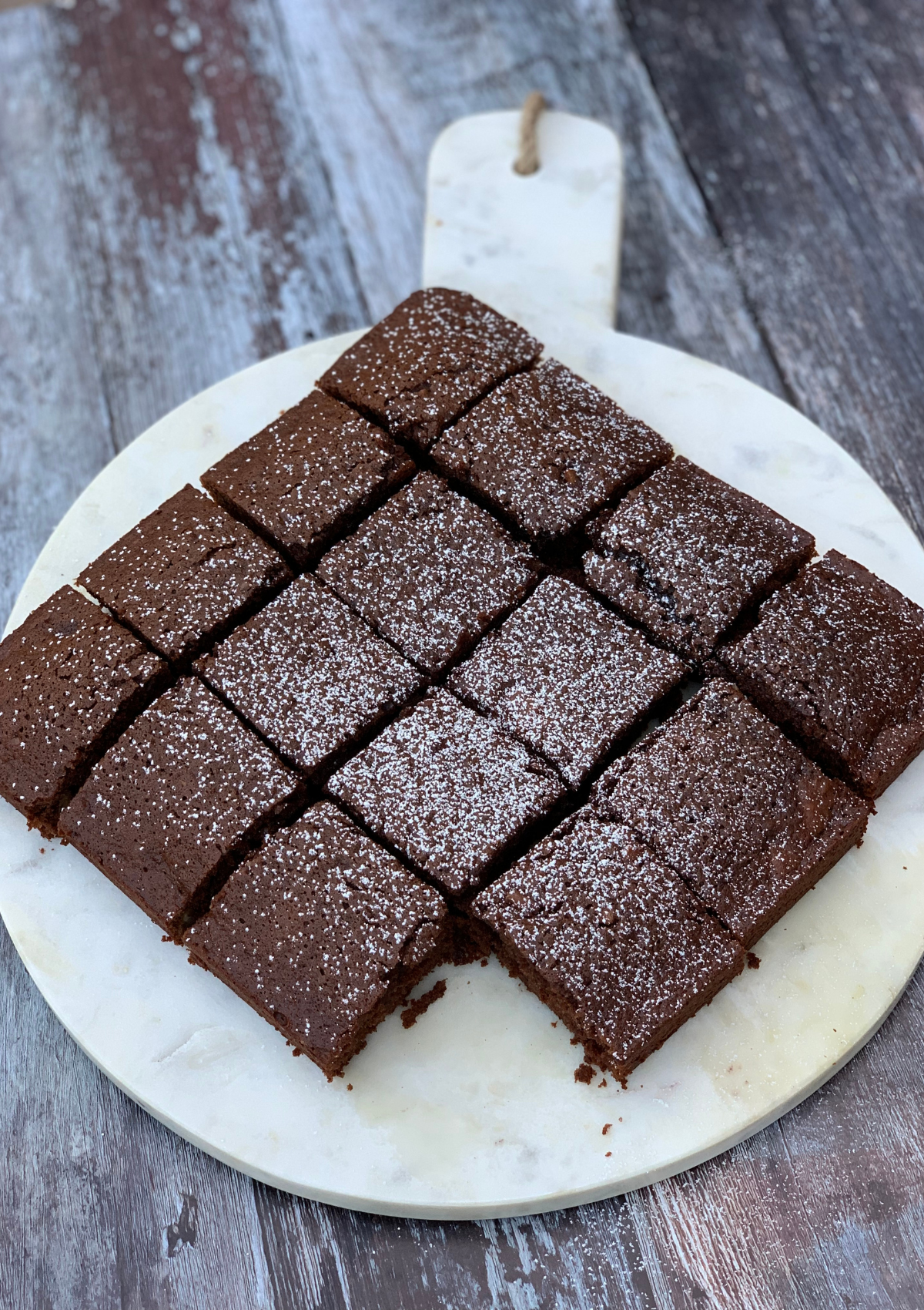 Applesauce Pecan Brownies cut but still together served on a round marble bread board. One brownie is missing. 
