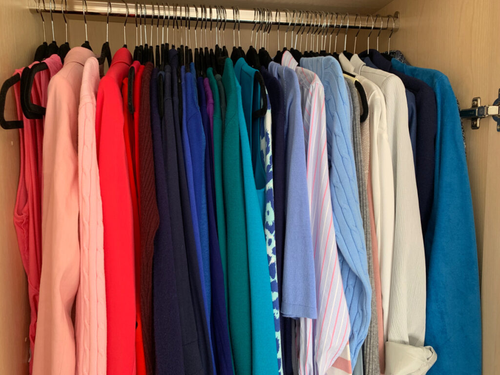 A wardrobe filled with clothes hanging up and organised by colour