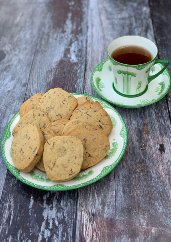Orange Pecan Cookies served on a china plate with a green design, cup of tea in the background