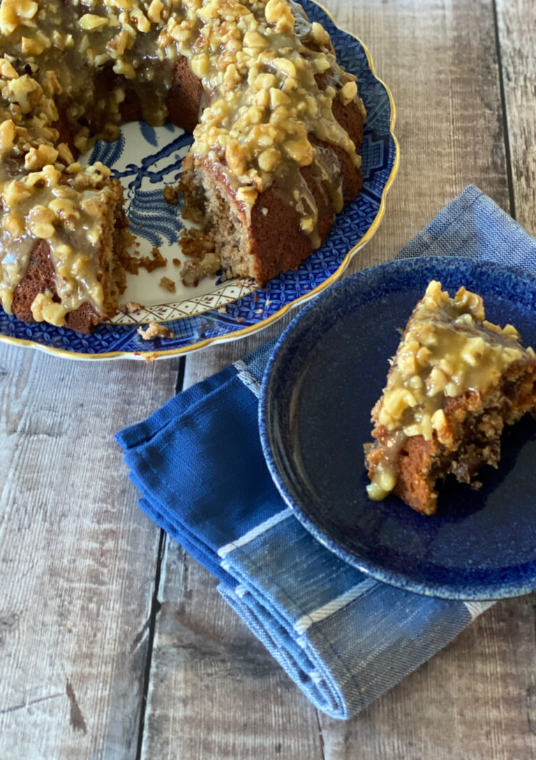Slice of Banana Date Cake with walnuts and dates on a plate in front of a whole cake