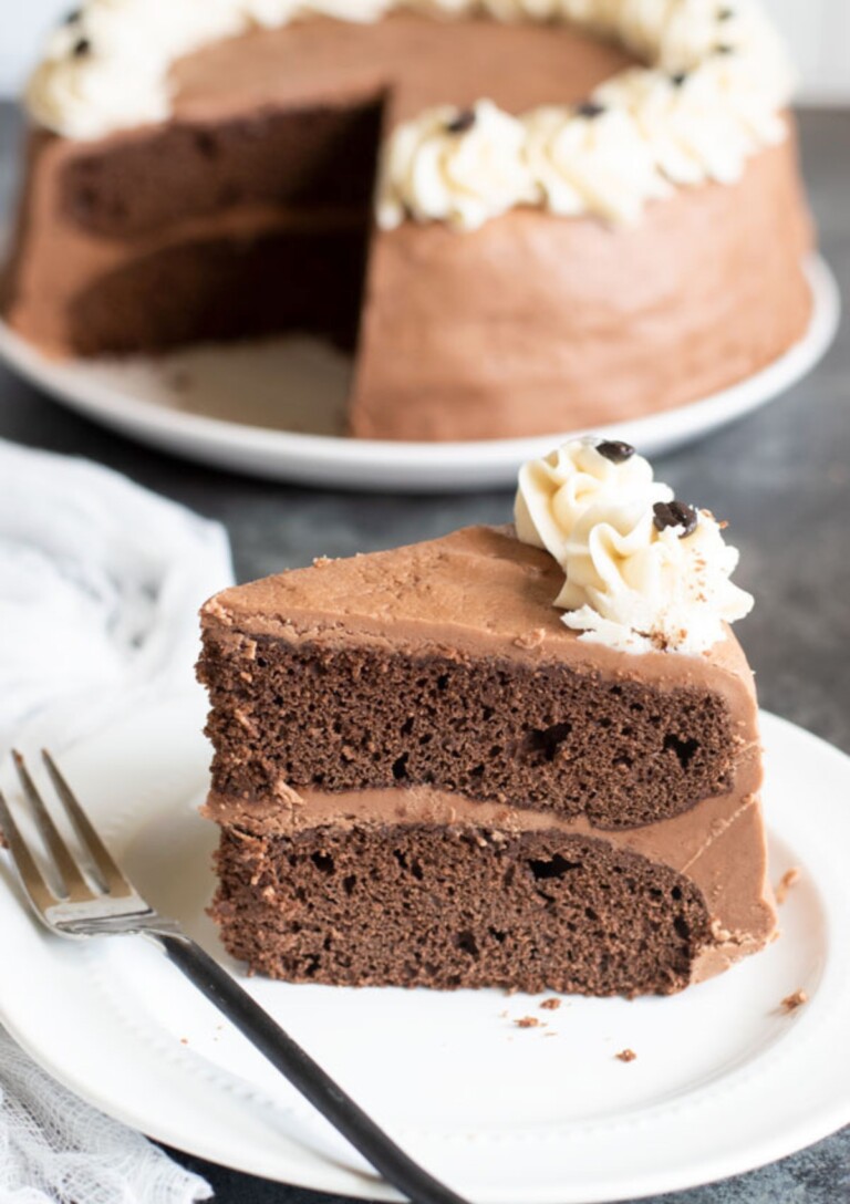A slice of Gluten-Free Mocha Cake sitting on a plate. The whole cake is in the background, missing one slice