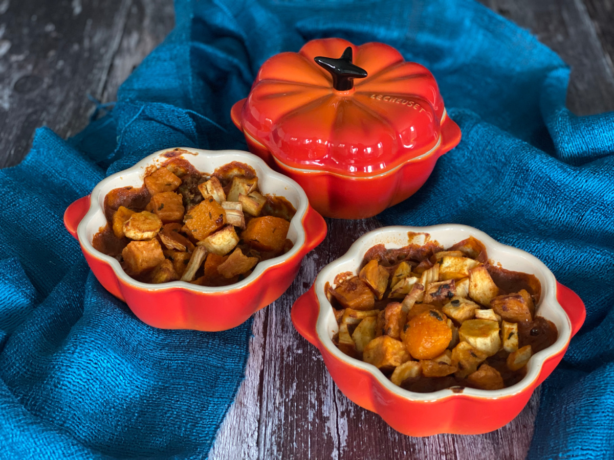 Two pumpkin shaped orange individual serving dishes of Cottage Pie with Roast Root Vegetables. There is a covered individual serving dish in the background.