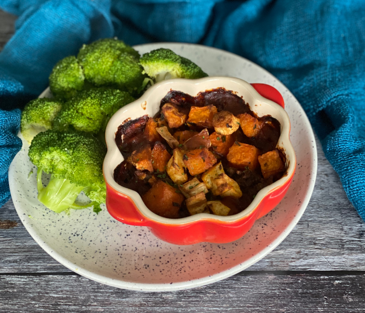Cottage Pie with a Roast Root Vegetable Topping served in an individual Le Creuset dish set on a white plate. Broccoli is served alongside.