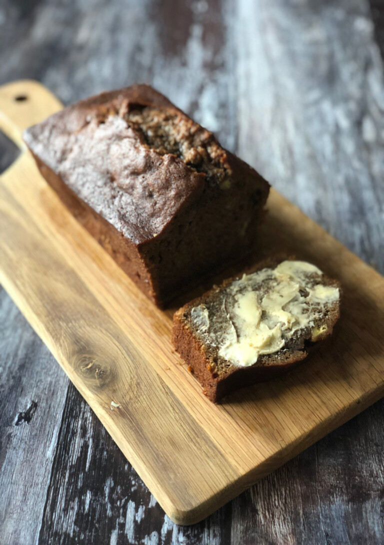 A loaf of Nigella's Italian Breakfast Banana Bread sliced and spread with butter, served on a bread board