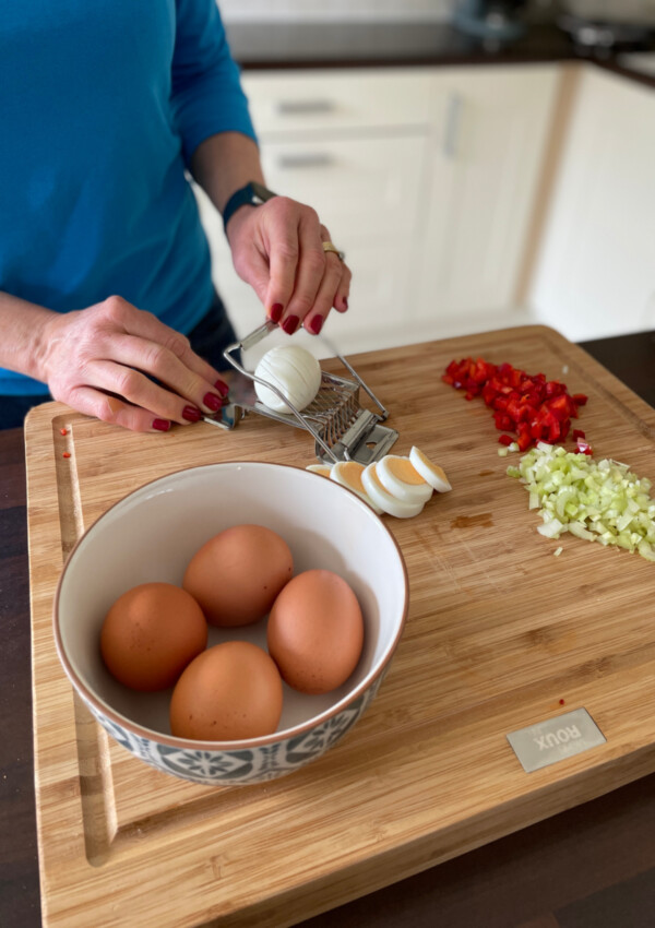 The ingredients for egg salad sandwiches - hard boiled eggs, chopped red pepper and celery on a wooden bread board