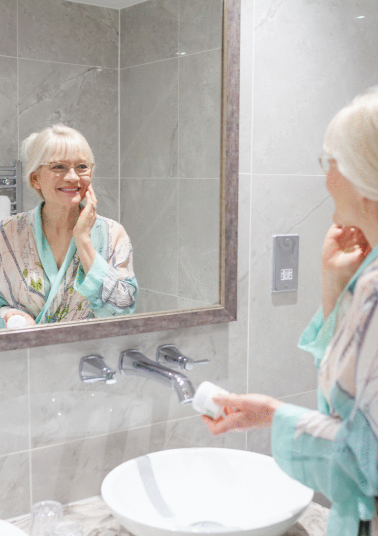 April J Harris reflected in a mirror. She is wearing a pastel dressing gown and applying moisturiser - Fall 2025 Beauty Tips