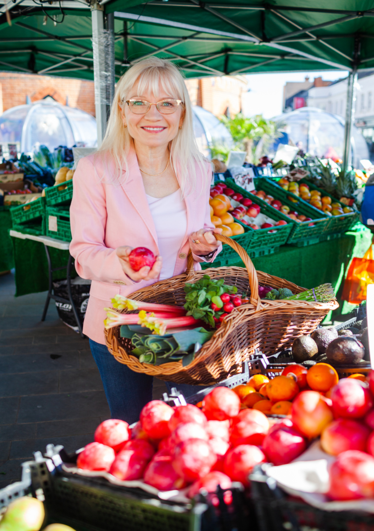 Easy Ways to Eat Less Meat - April J Harris in an outdoor farmer's market choosing fruit and vegetables to put in her market basket