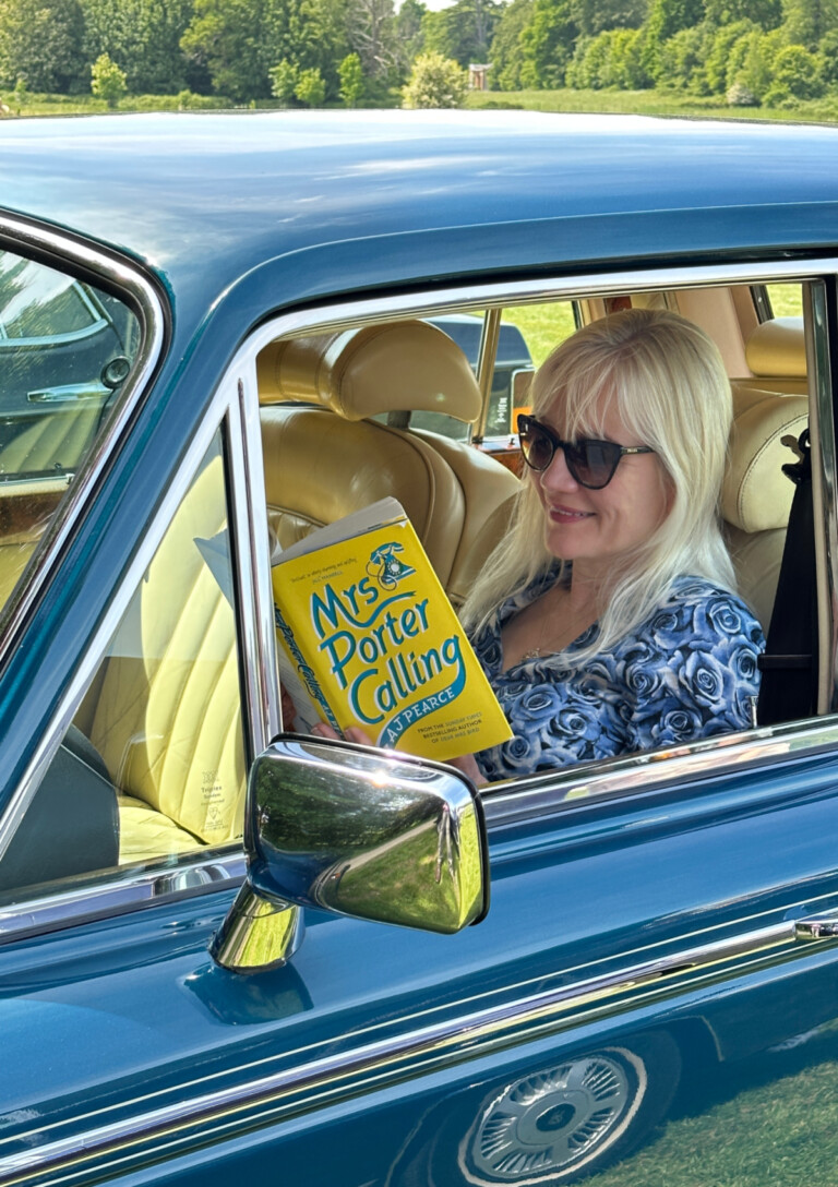 April Harris sitting in a car reading Mrs Porter Calling, a third instalment in the Emmy Lake Chronicles, is an historical fiction novel about life on the home front in WWII.
