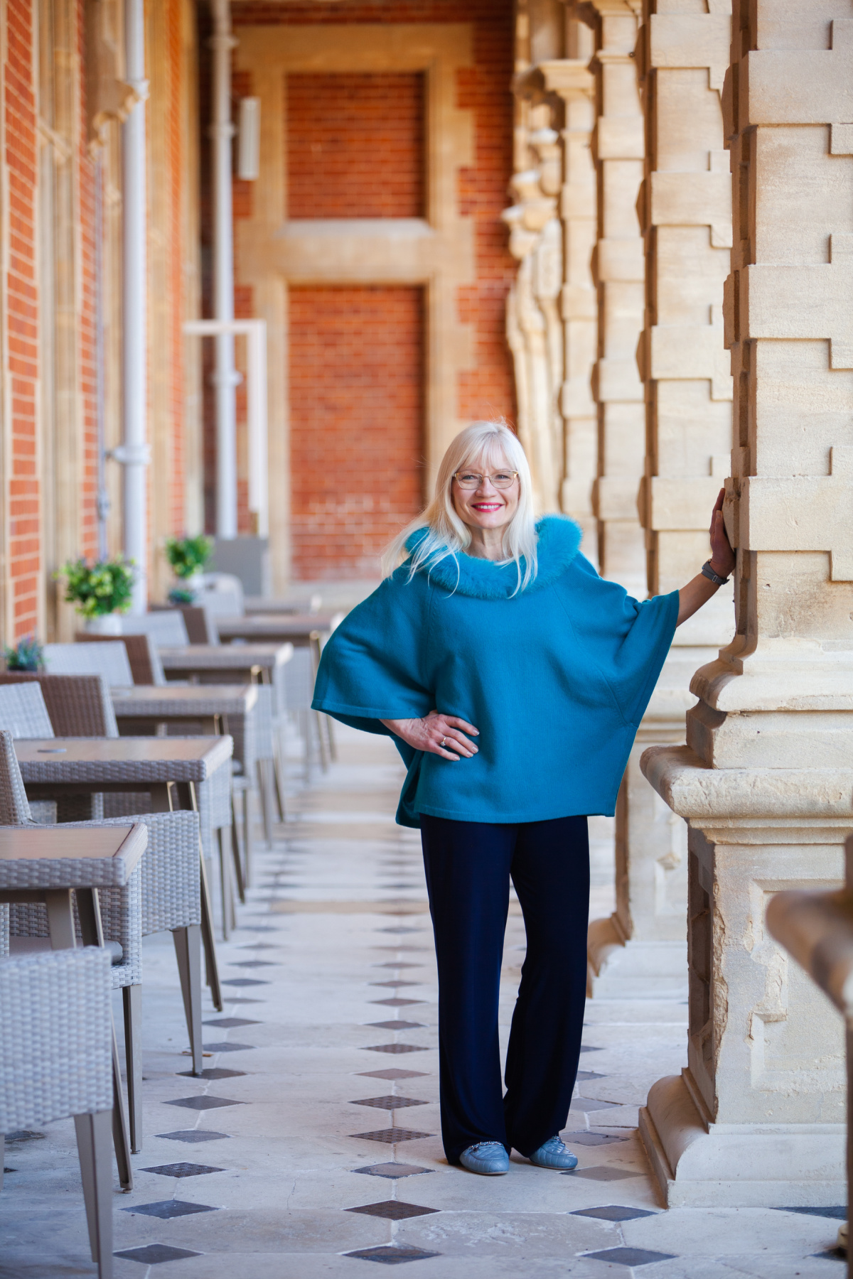 Adding colour to your wardrobe - April J Harris wearing a turquoise poncho and standing by a pillar 