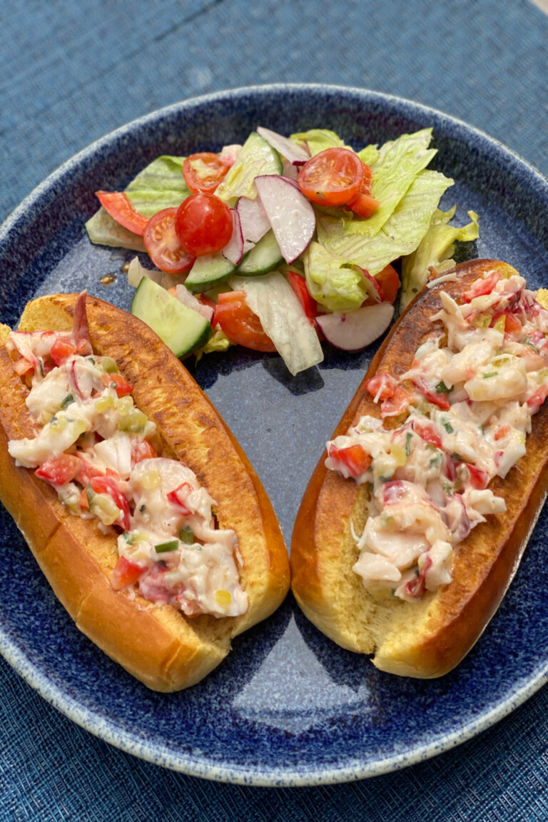 Two Lobster Rolls served on a plate with a side of salad