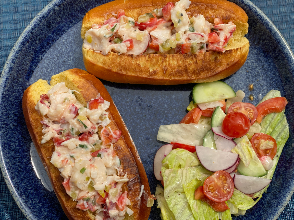 Lobster rolls served on a blue plate with a side of salad