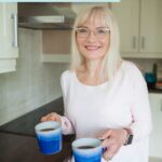 A woman holding two coffees in her kitchen September 2023 edition Hearth and Soul