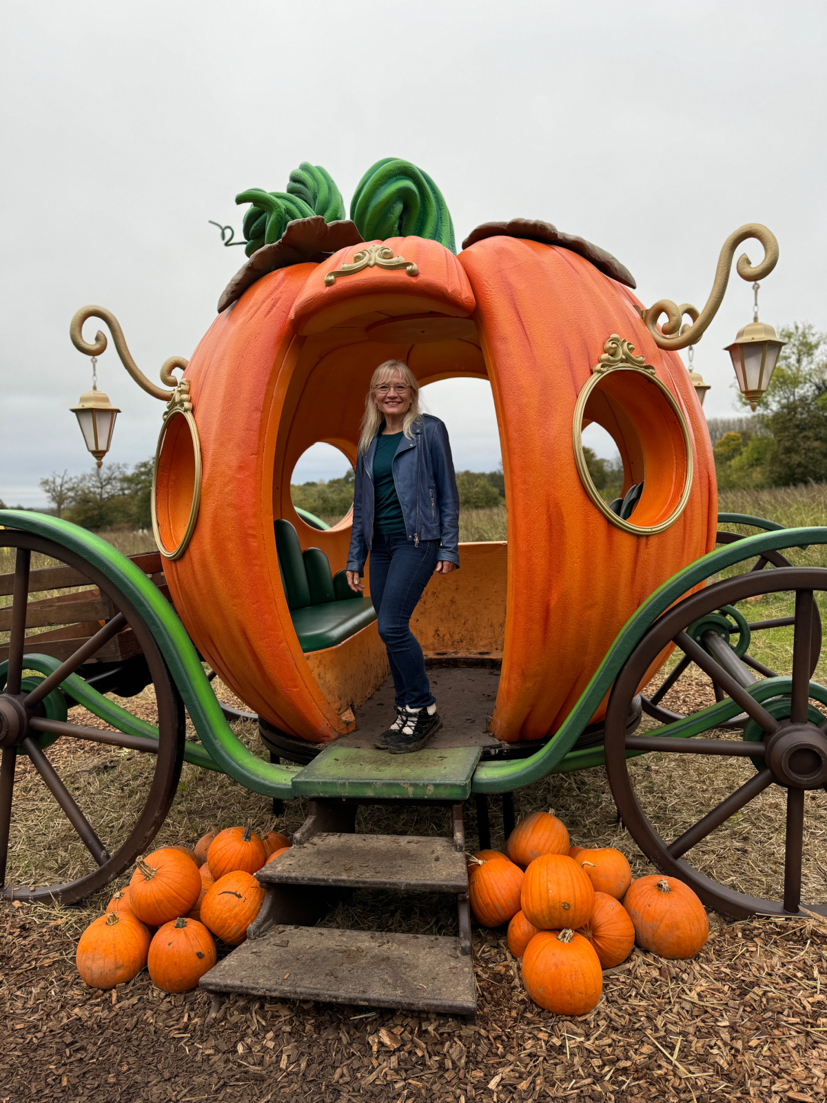 A photograph of April Harris in a decorative pumpkin coach on a field. 